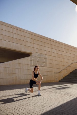 Photo for Athletic woman in sportswear stretching legs before doing workout outside in morning - Royalty Free Image