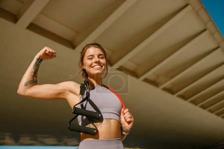Smiling athletic woman in sportswear with a resistance band slung around her neck standing outdoors