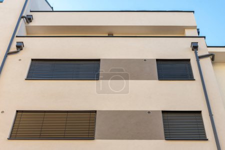 Foto de Tuberías de desagüe en la pared de un moderno edificio residencial de varios pisos, las ventanas están cubiertas con persianas de madera - Imagen libre de derechos