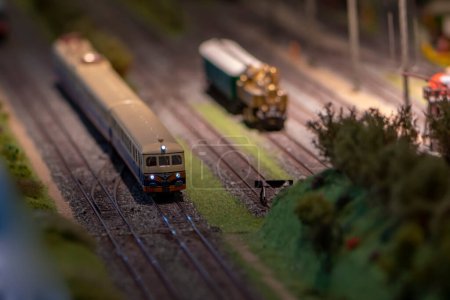 Photo for A passenger train with its headlights on rides on rails, a toy train stands on a siding at a dead end, selective focus. - Royalty Free Image
