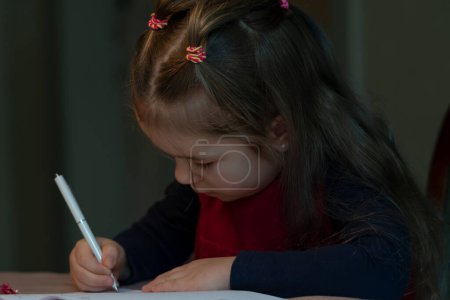 Foto de Una niña dibuja en papel sentado en una mesa, tonalidad oscura. - Imagen libre de derechos
