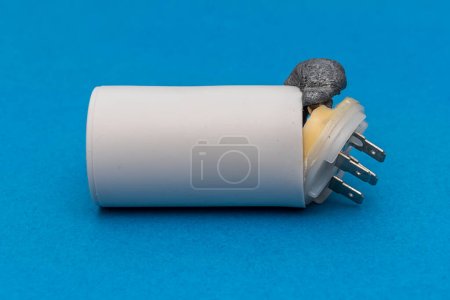 Photo for Faulty electric starting capacitor for electric motors on a blue background. The internal composition in the form of foam tore off the lid and came out. - Royalty Free Image