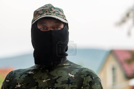 Téléchargez les photos : Un homme en uniforme militaire et cagoule regarde la caméra. Concept : mobilisation dans l'armée, mercenaire au front, guerre en Ukraine. - en image libre de droit