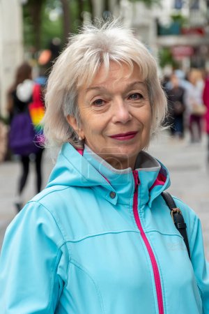 Foto de Retrato de feliz anciana de 60-70 años sobre fondo borroso de la calle, multitud de personas, fondo borroso de la ciudad europea. - Imagen libre de derechos