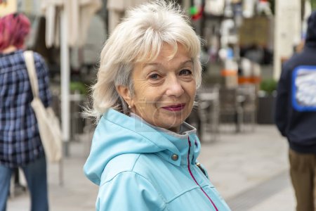 Foto de Retrato callejero de una anciana de 65-70 años sobre el fondo borroso de la calle y multitudes de personas en una ciudad europea. - Imagen libre de derechos