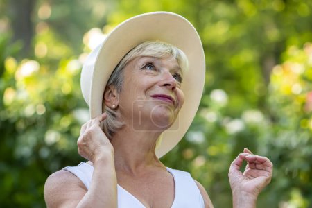 Retrato emocional de una mujer de 60-70 años hermosa rubia en un sombrero de paja en el fondo de la naturaleza.