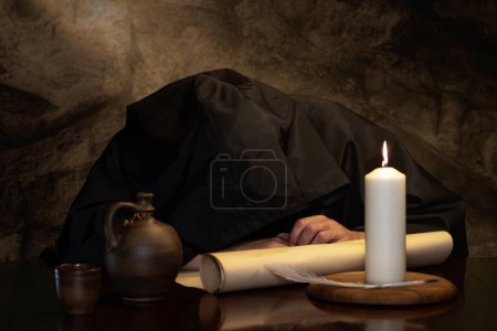 Téléchargez les photos : Un moine en soutane noire s'est endormi ivre à une table avec une cruche de vin dans une auberge médiévale. Concept : ivresse et alcoolisme. - en image libre de droit