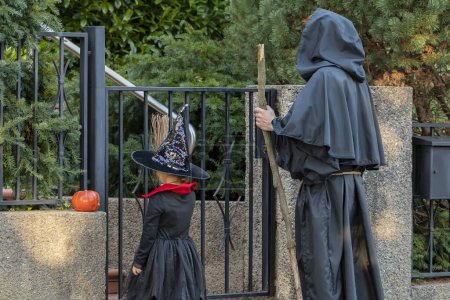Photo for A girl witch with a broom and a man monk standing at the entrance of a house. Concept: sweets or nasties, Halloween games and activities, festive ritual. - Royalty Free Image