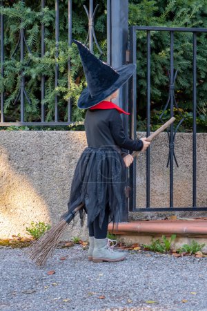 Téléchargez les photos : Une fille en costume de sorcière avec un balai et un chapeau attend des bonbons et des bonbons à l'entrée de la maison. Fête d'Halloween d'automne. - en image libre de droit