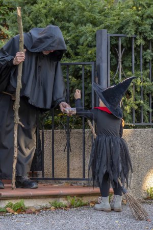 Photo for Hallowen holiday, a man dressed as a monk gives a girl dressed as a witch a candy. - Royalty Free Image