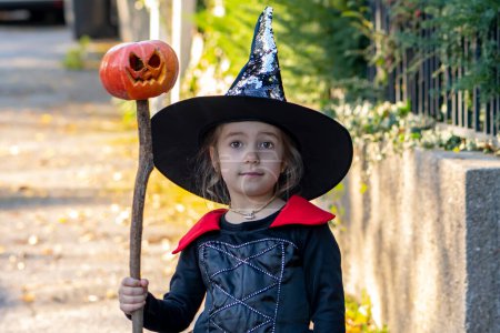 Téléchargez les photos : Portrait d'une jeune fille habillée en sorcière Veolia avec balai et chapeau, citrouille d'Halloween posée sur un bâton. Concept : Toussaint, Halloween, spectacle costumé. - en image libre de droit