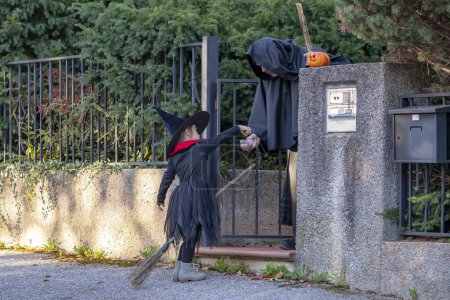 Photo for A girl in a witch costume receives sweets from a male monk at the entrance to the house. Concept: sweets or nasties, Halloween games and activities, fun holiday ritual. - Royalty Free Image
