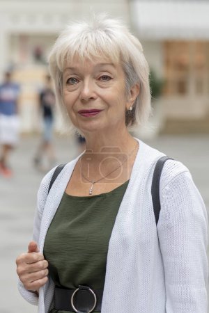 Foto de Retrato de mujer sonriente de 65-70 años sobre fondo borroso de la calle europea, foto vertical. - Imagen libre de derechos
