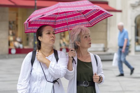 Téléchargez les photos : Deux femmes âgées et d'âge moyen marchent sous un parapluie dans une ville européenne. Concept : tourisme et voyages, amitié féminine, relations familiales. - en image libre de droit