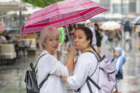 Téléchargez les photos : Deux femmes d'âges différents marchent sous un parapluie dans une ville européenne. Concept : tourisme et voyages, amitié féminine. - en image libre de droit