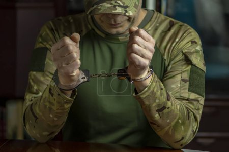 Photo for A soldier in camouflage uniform, hands cuffed, sits at a desk. - Royalty Free Image