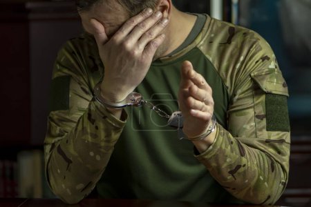 Photo for Portrait of a handcuffed uniformed military man hiding his face, dark tonality. - Royalty Free Image