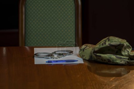 Photo for On the table is a camouflage military cap, army medallions, police handcuffs and a blue pen with a piece of paper. Concept: law enforcement, military authority. - Royalty Free Image