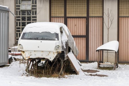 Abandoned and disassembled car in the snow by the old garage, long repair.