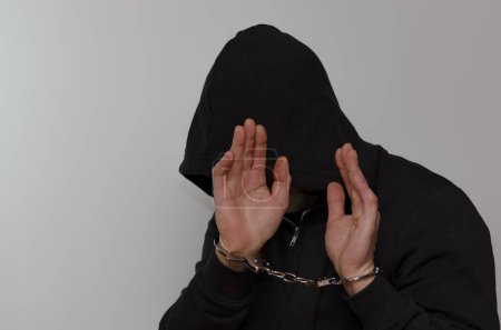 Photo for A handcuffed man hides his face in the hood of a hoodie. - Royalty Free Image