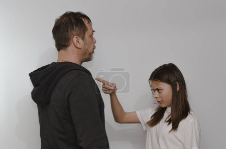 A teenage girl argues with her father on a light background.