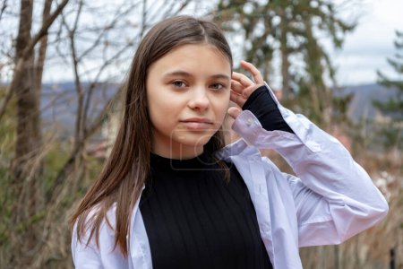 Ein 12-jähriges Mädchen fixiert ihre langen Haare im Hintergrund eines Landhauses und einer Landschaft.