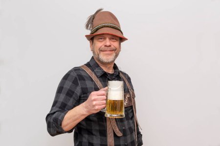 Porträt eines älteren Mannes mit Tirolerhut und Lederhose, der ein Glas Bier auf weißem Hintergrund hält.