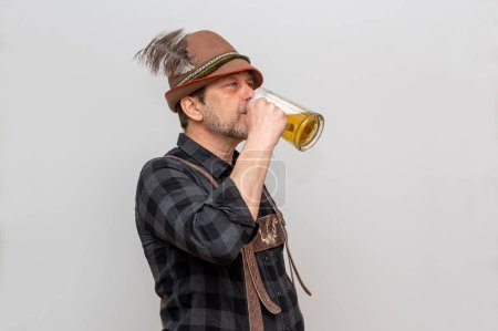 Studioporträt eines älteren bärtigen Mannes mit Hut, der Bier mit Schaum auf hellem Hintergrund trinkt.