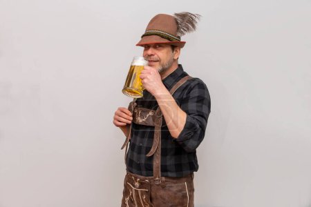 Porträt eines älteren, bärtigen Mannes mit Tirolerhut, der ein Glas Bier mit Schaum vor weißem Hintergrund hält.