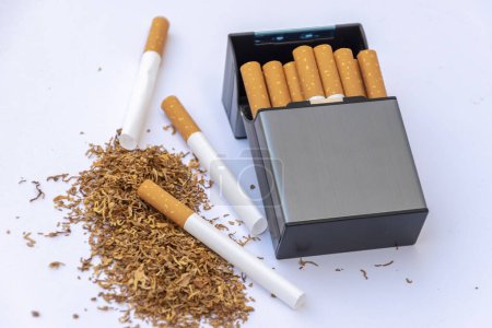 Cigarrillo junto a tabaco para fumar disperso y carcasas de cigarrillos vacías sobre un fondo blanco.