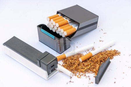 Handgerät zum Füllen von Zigarettendosen mit Tabak, verstreuten leeren Zigaretten und einem Stapel Tabak auf weißem Hintergrund, Zigarettenetui mit selbstgemachten Zigaretten.