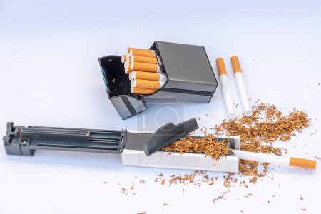 A cigarette case in a stuffing machine filled with tobacco, empty cigarettes and a cigarette case with homemade cigarettes.