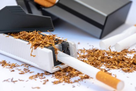 Eine Zigarettenschatulle, die in eine Füllmaschine gesteckt und mit Tabak, leeren Zigaretten und einer Zigarettenschatulle mit selbstgemachten Zigaretten gefüllt wurde.