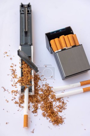 Stuffing machine for cigarette casings filled with tobacco, empty cigarettes on white background, cigarette case with homemade cigarettes.