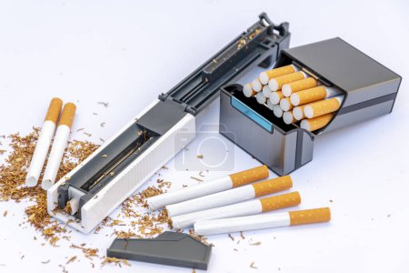 Stopfmaschine für Zigarettendosen mit Tabak, verstreut leere Zigaretten und ein Stapel Tabak auf weißem Hintergrund, Zigarettenetui mit selbstgemachten Zigaretten.