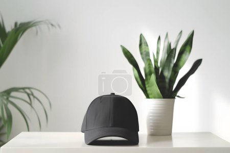 Black baseball cap on white table and green plant in the backgro