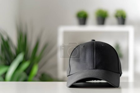 Black baseball cap on white table with green plant background. M