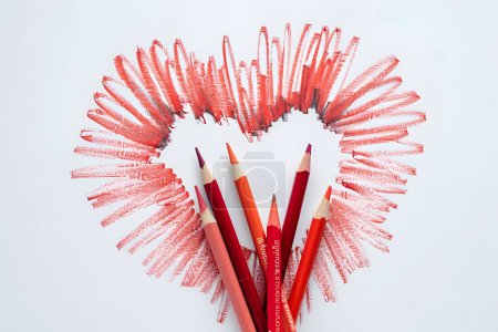 Red pencils in the scratch shape of heart on a white paper backg