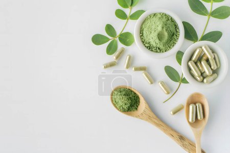 Cápsulas de hierbas medicinales y polvo verde en cuchara de madera en whi