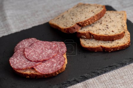 Téléchargez les photos : Salami tranché et laitue sur fond noir, vue de dessus. sandwichs ouverts avec saucisse de salami tranchée sur pain de seigle - en image libre de droit