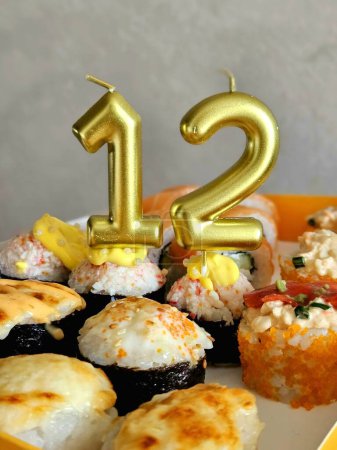 Téléchargez les photos : Rouleaux avec bougies de vacances. délicieux plats japonais, gros plan délicieux et sains rouleaux de sushi. bougies à gâteau avec numéro 12 - en image libre de droit