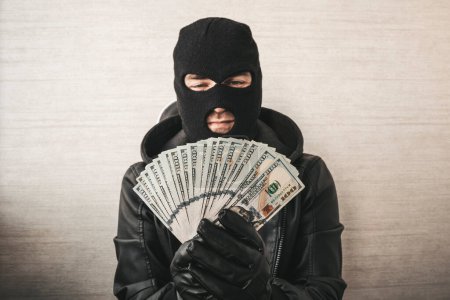 Primer plano retrato de ladrón astuto con máscara negra y guantes contando dinero sobre fondo blanco. centrarse en el dinero.