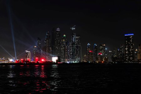 Foto de El horizonte de Dubai Marina después del atardecer con un mar en primer plano. Hermosa vista nocturna de los rascacielos de Dubai desde el mar. - Imagen libre de derechos
