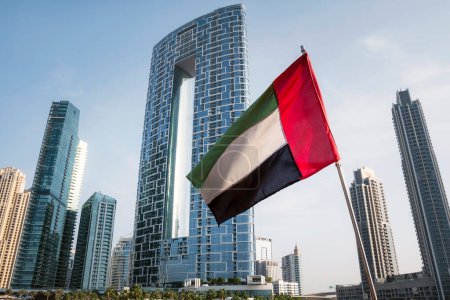 Foto de Vista única de los Emiratos Árabes Unidos, bandera nacional de los Emiratos Árabes Unidos ondeando en el aire con el horizonte de Dubái en el fondo. Día Nacional de los EAU - Imagen libre de derechos
