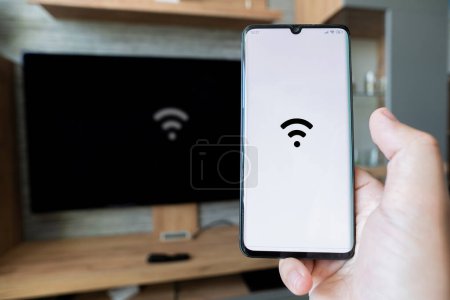 Photo for Male hand holding a smartphone. Control TV with smartphone. connectivity between smart tv and smart phone through wifi connection. to distribute the Internet through wifi from phone to computer - Royalty Free Image