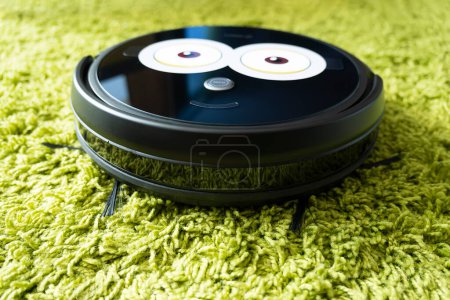 Photo for Automatic robot vacuum cleaner in black on a green floor . New modern technologies for apartment cleaning. smart home electronic assistant - Royalty Free Image