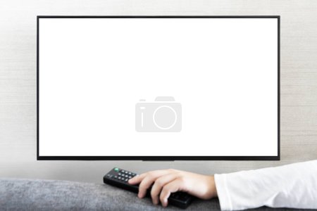 Photo for TV remote control in male hand in front of widescreen TV set with blank screen on white wall background. guy switches channels on the remote from the TV. - Royalty Free Image