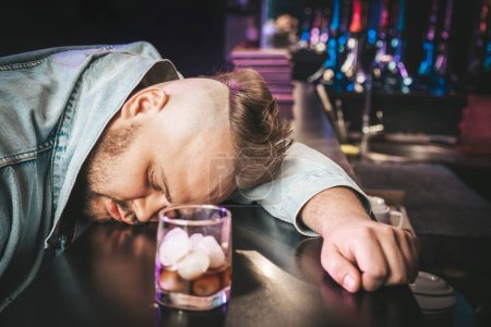 Foto de Alcoholismo, joven deprimido dormir en la mesa mientras bebe bebidas alcohólicas, vaso de whisky solo por la noche. Tratamiento de la adicción al alcohol, sufren abuso problema alcoholismo concepto - Imagen libre de derechos