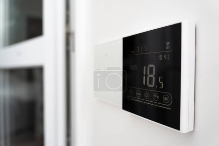 Téléchargez les photos : Écran de climatiseur sur le mur qui montre une température de l'air de 18 degrés Celsius. un dispositif de commande du chauffage par le sol. - en image libre de droit