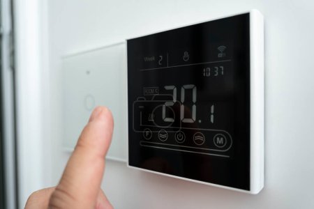 Foto de Primer plano de una mano masculina que ajusta un termostato digital moderno montado en la pared. 20 grados centígrados habitación temperatura cómoda. termómetro electrónico en la pared - Imagen libre de derechos